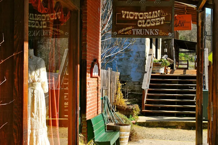 A vintage shop sign reads Victorian Closet above a sidewalk. A mannequin in a white dress stands inside the store window. Wooden steps, benches, and rustic buildings appear in the background.