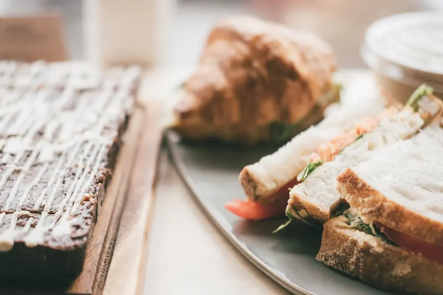 Close-up of a plate with sandwiches, a croissant, and a bowl, next to a wooden board holding a chocolate dessert with white drizzle. Close-up of a plate with sandwiches, a croissant, and a bowl, next to a wooden board holding a chocolate dessert with white drizzle.